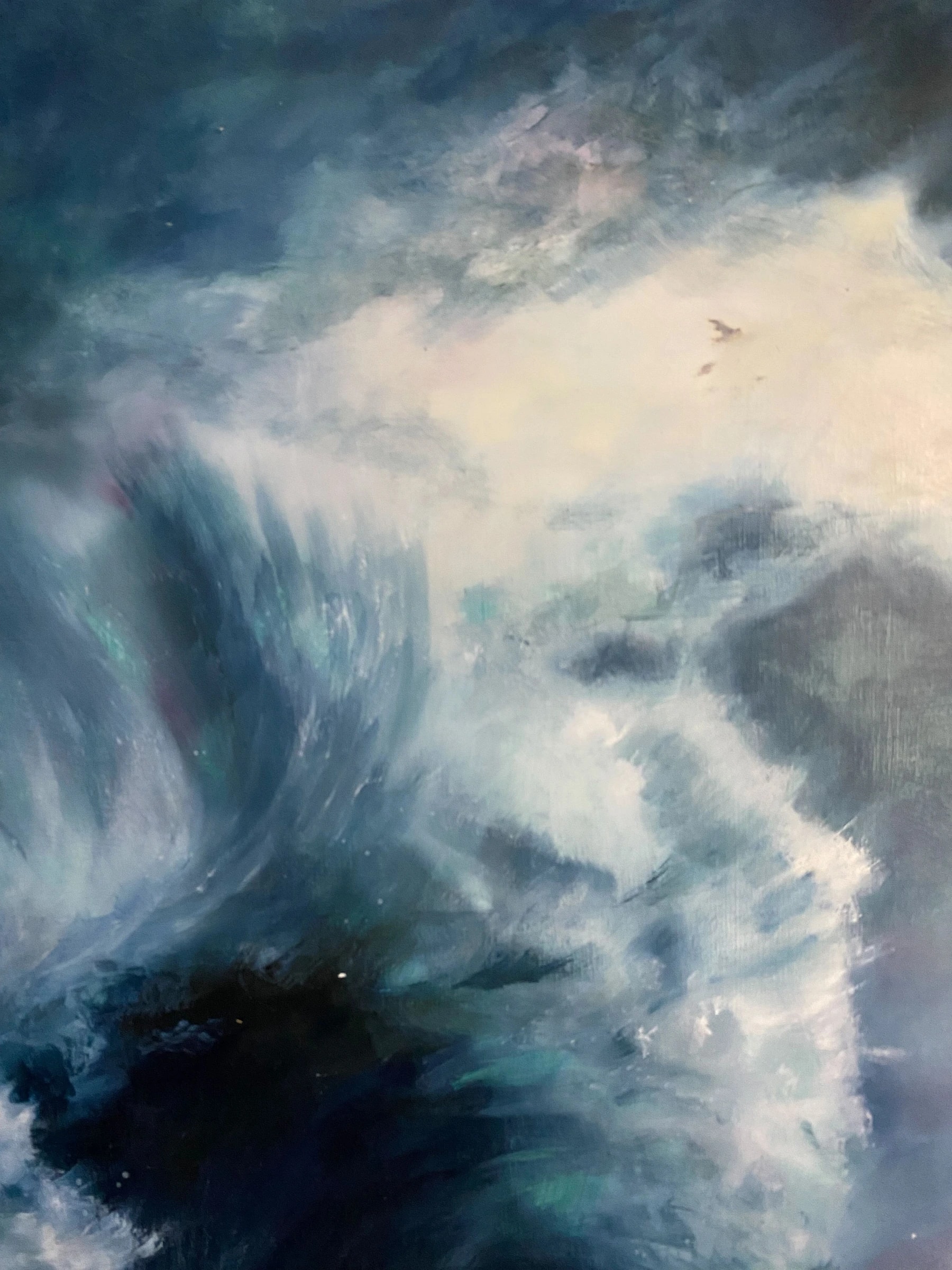 Soft seascape of spray and foam rising at right, pale cream light opening across the sky, and one small dark bird gliding over blue-grey water.